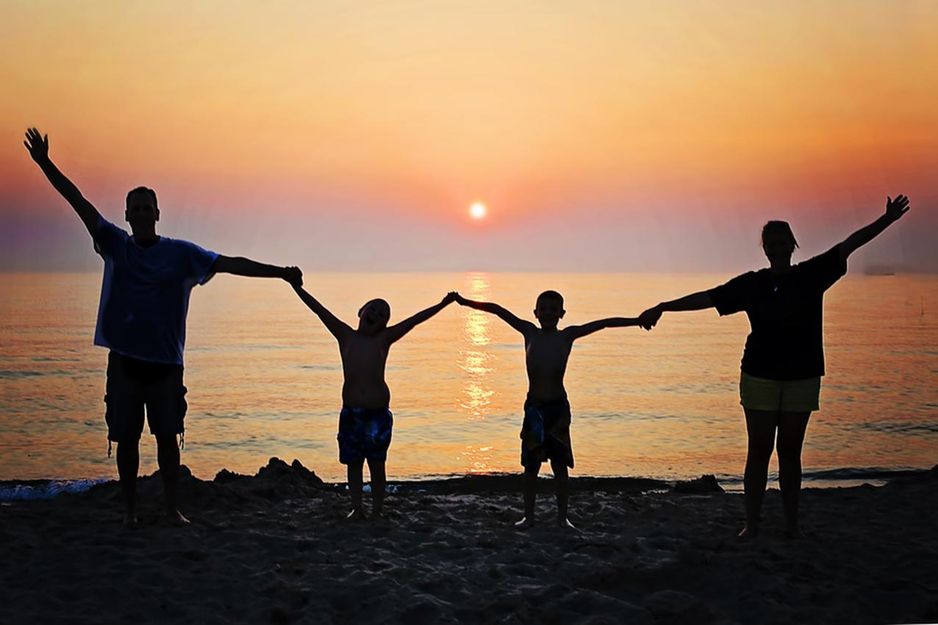 Familie hält sich bei Sonnenuntergang am Strand an den Händen.